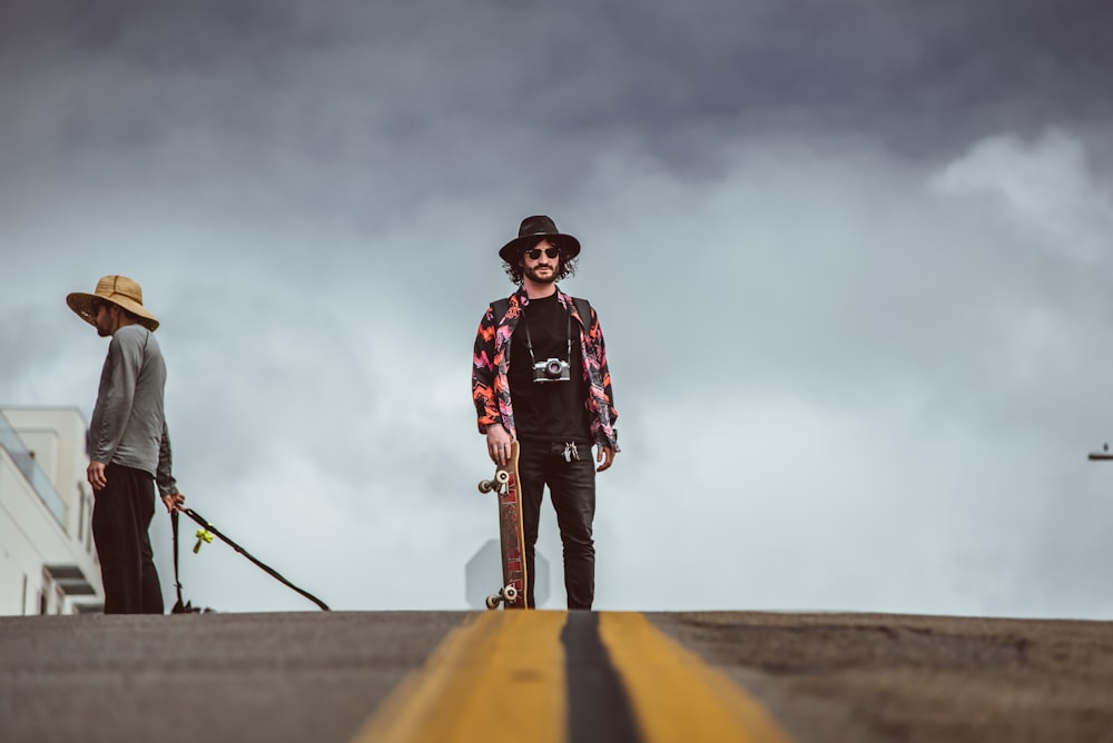 man holding skateboard while standing in the middle of road