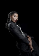 Stylish woman wearing a black dress with white gold jewelry, posing against a soft black backdrop.