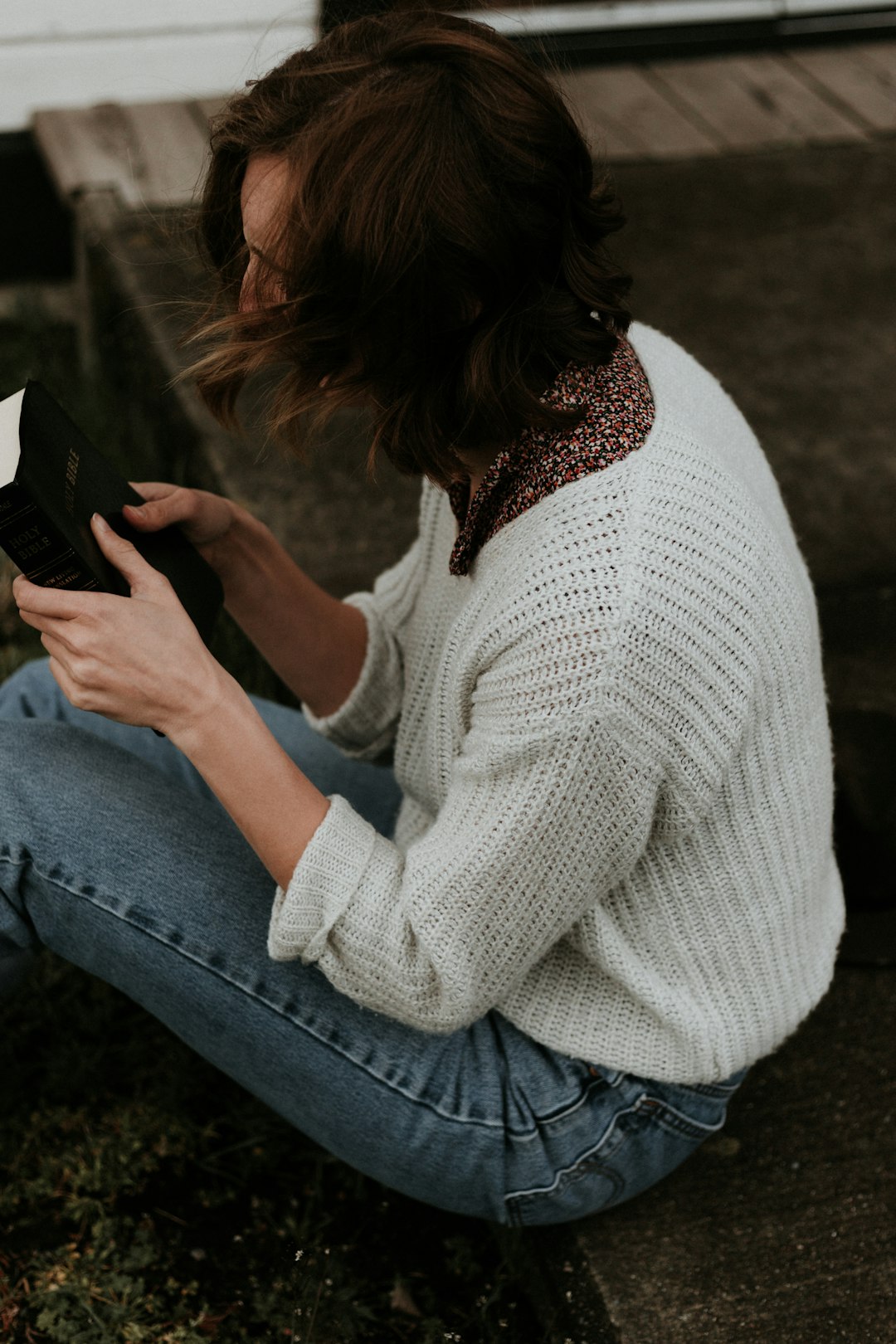 woman holding book sitting on brown concrete pathway