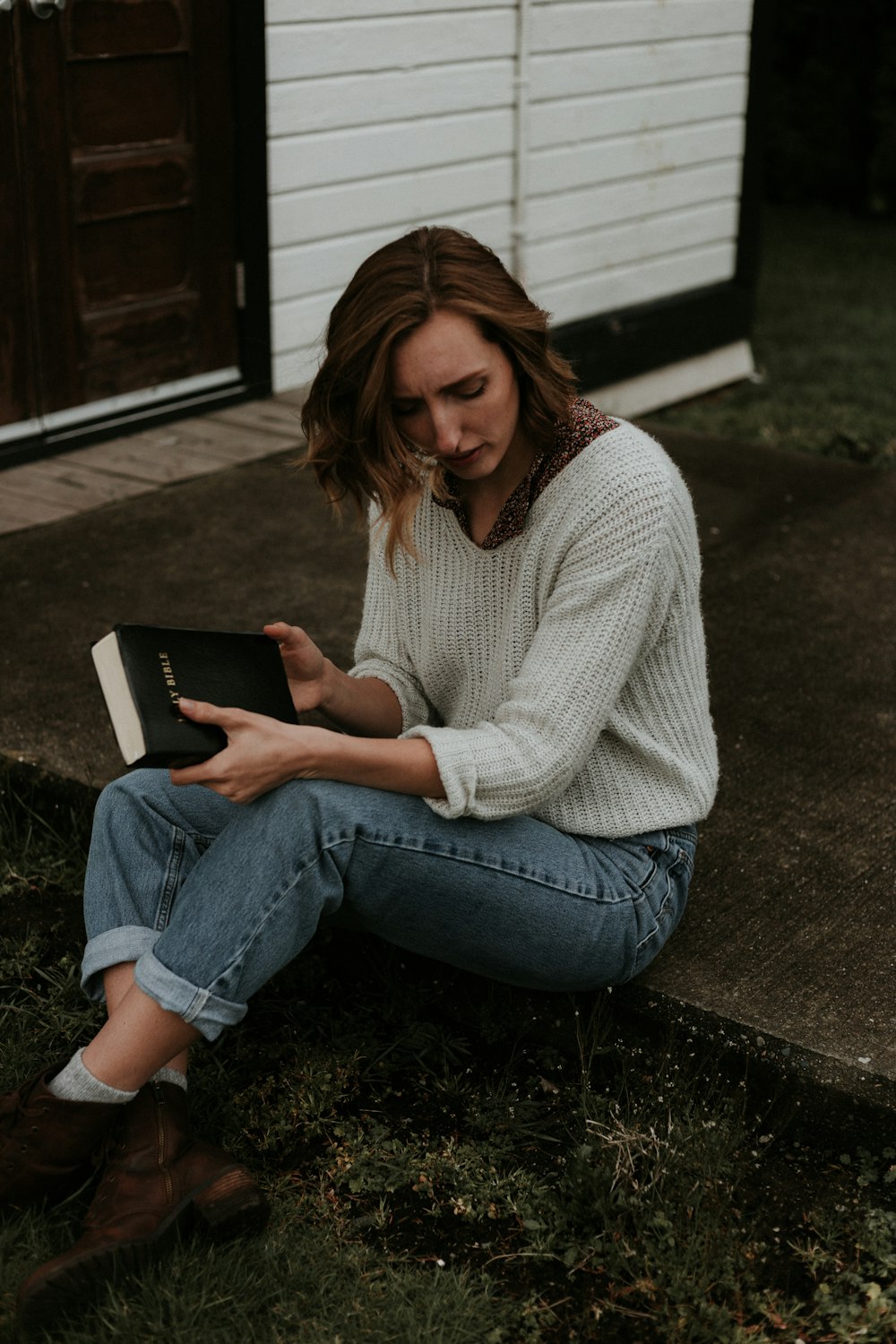 woman carrying book sitting on brown concrete pathway