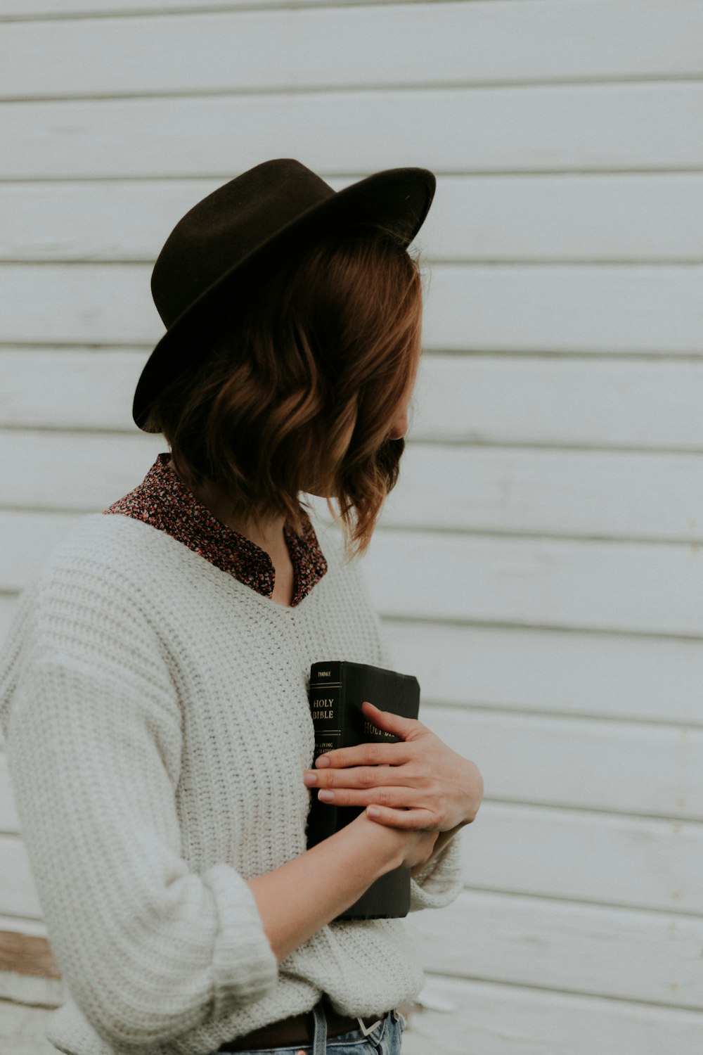 woman holding book standing near white wooden wall