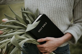 person carrying Holy Bible and bunch of green leaves