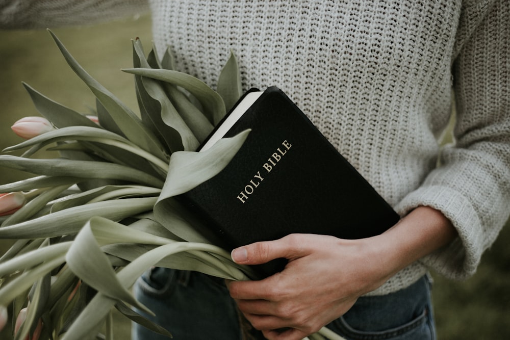 person carrying Holy Bible and bunch of green leaves