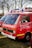A red fire service vehicle with the words 'FEUERWEHR' and 'Jugendfeuerwehr Mindelheim' painted on the side. The vehicle has a Volkswagen emblem on the front. It is parked outdoors on grass with other vehicles nearby. There are emergency lights and loudspeakers mounted on the roof.