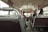 A vintage-style bus interior with metal handrails and wooden floorboards. Several passengers, including adults and a child, are seated and facing forward. The atmosphere inside is calm, with muted lighting and slightly worn upholstery.