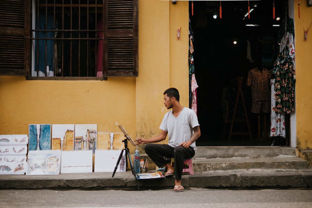 man sitting on concrete stairs near beige building