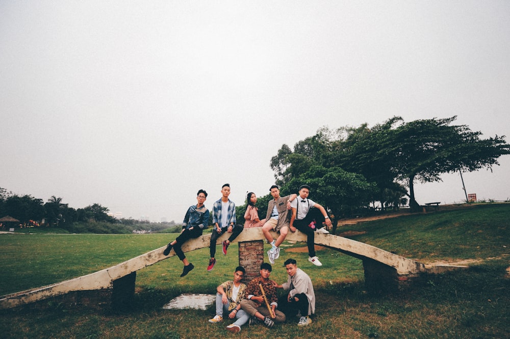 five person sits on white bridge over three men sits on grass field