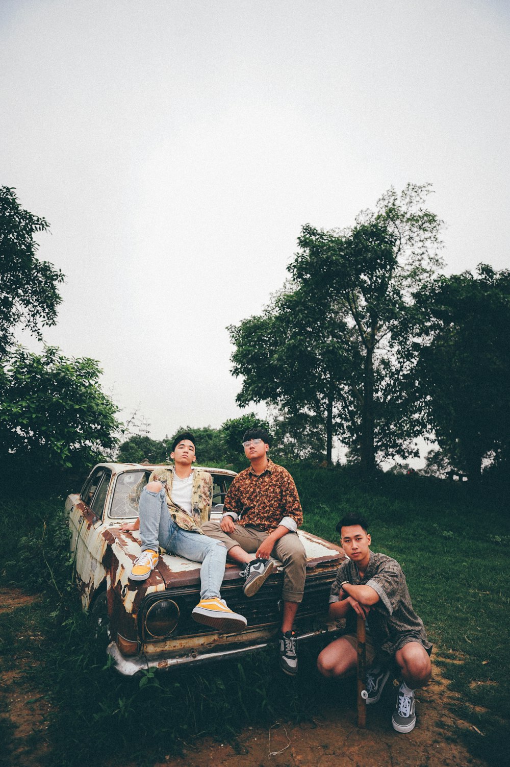 man kneeling beside wrecked car with two men sitting on hood