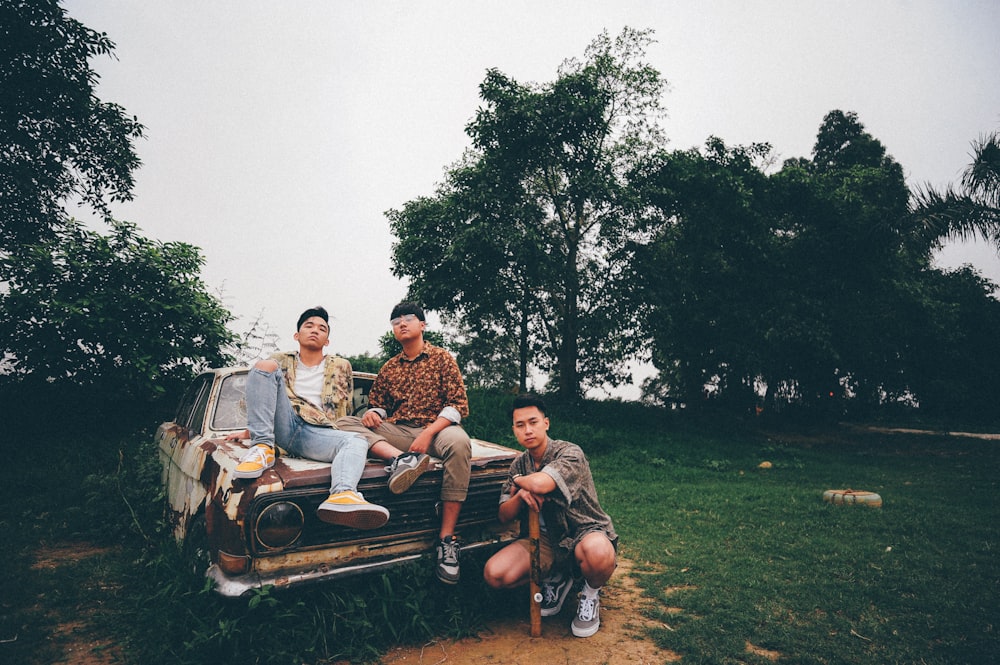 three sitting on white classic car on field