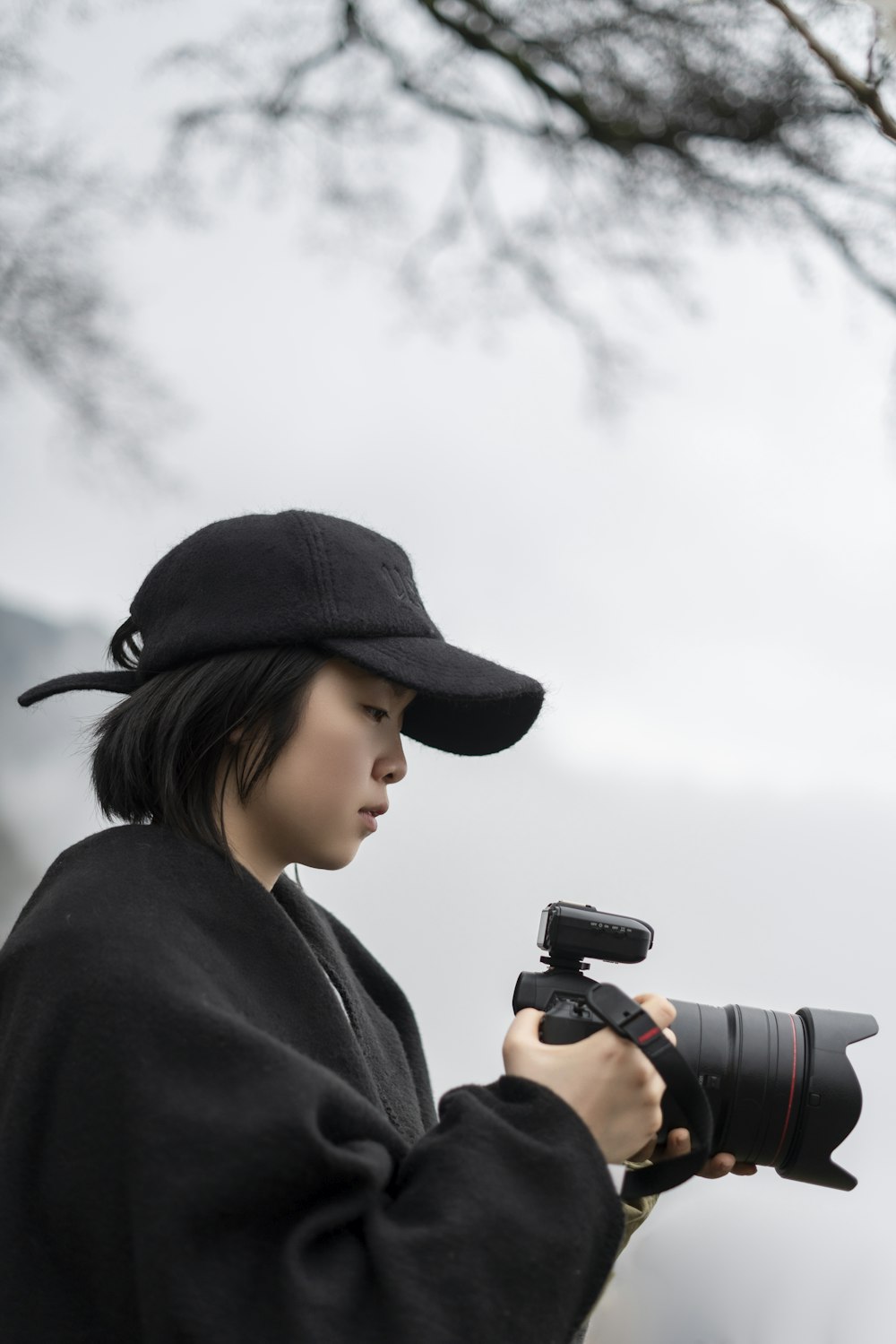 femme portant une casquette noire tenant un appareil photo noir