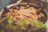A dish consisting of seafood, including shrimp and mussels, is displayed in a pan. The meal is likely a type of paella or similar rice dish, as rice grains and other ingredients are visible. The image has a soft focus effect, creating a warm and inviting atmosphere.