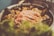 A dish consisting of seafood, including shrimp and mussels, is displayed in a pan. The meal is likely a type of paella or similar rice dish, as rice grains and other ingredients are visible. The image has a soft focus effect, creating a warm and inviting atmosphere.