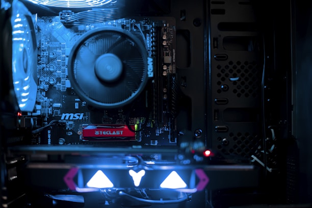 A close-up view of a computer's internal components, featuring a large CPU fan and several illuminated circuit boards. The lighting casts a bluish glow, highlighting the intricate details and branding of the motherboard, including labels like 'MSI' and 'AMD'.