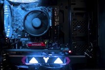 A close-up view of a computer's internal components, featuring a large CPU fan and several illuminated circuit boards. The lighting casts a bluish glow, highlighting the intricate details and branding of the motherboard, including labels like 'MSI' and 'AMD'.