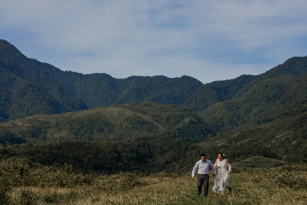 couple running on grass field surrounded by terrain