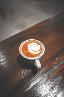 Close-up of a warm cappuccino with frothy milk art, resting on a rustic wooden table surrounded by soft garden light.
