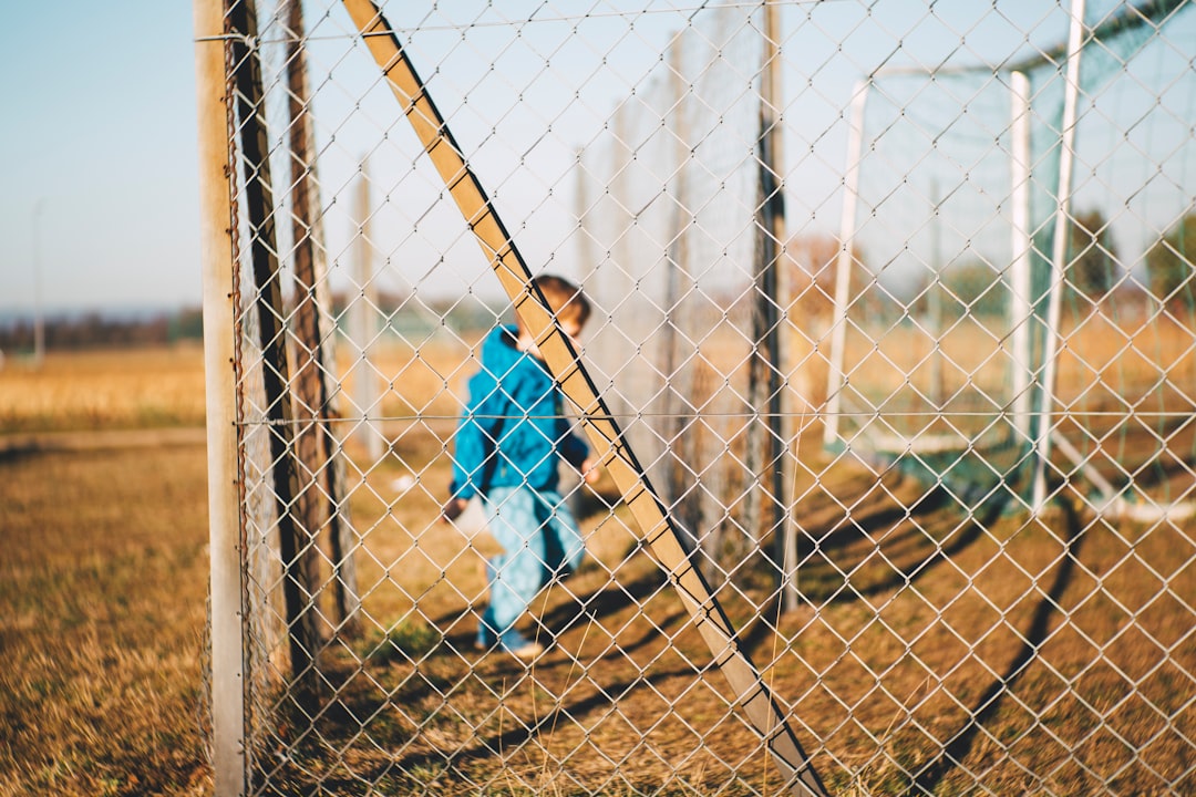 boy standing inside cyclone fences during daytime