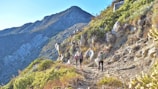 Hikers walking along a rocky trail beside the Atlas Mountains on a sunny day.