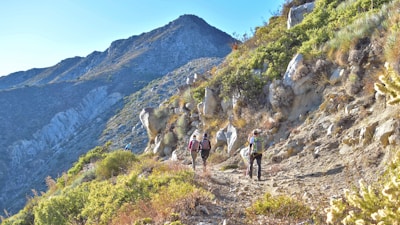 Hikers walking along a rocky trail beside the Atlas Mountains on a sunny day.