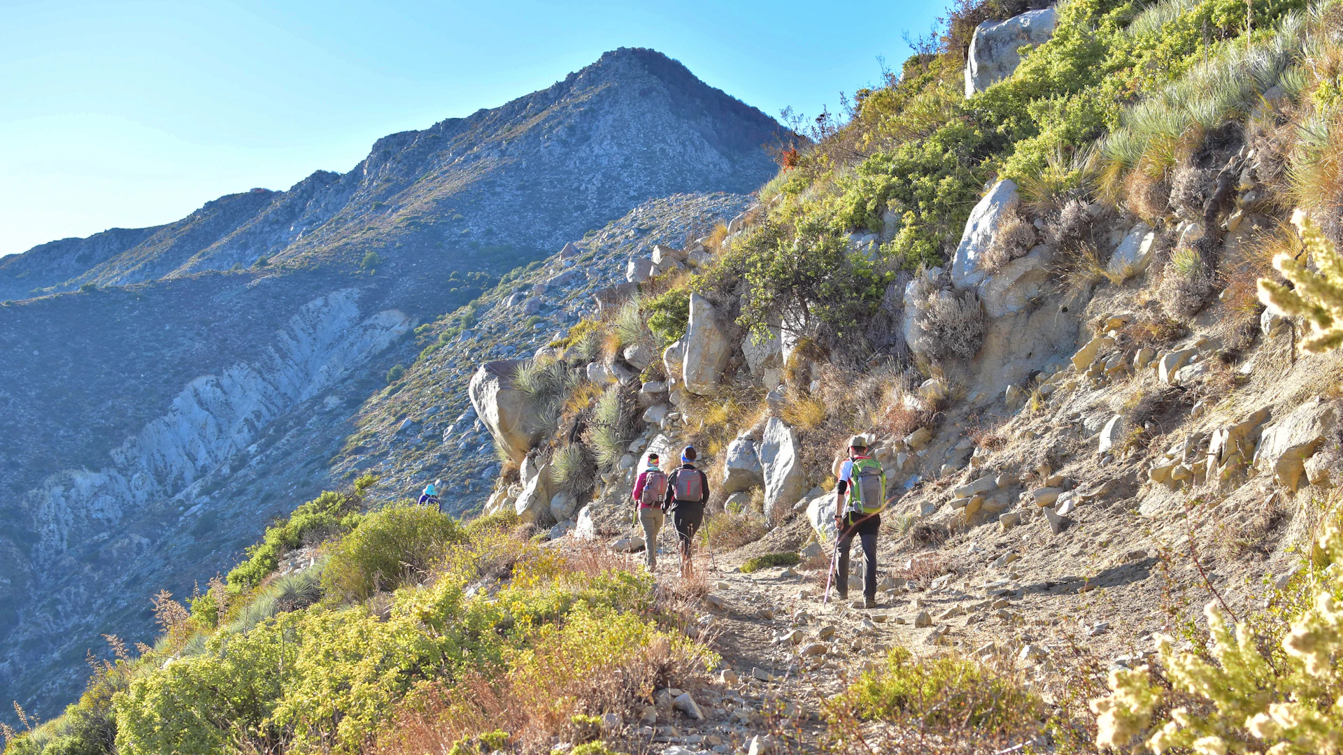 Hikers walking along a coastal trail near Chefchaouen, with the blue city visible in the background.