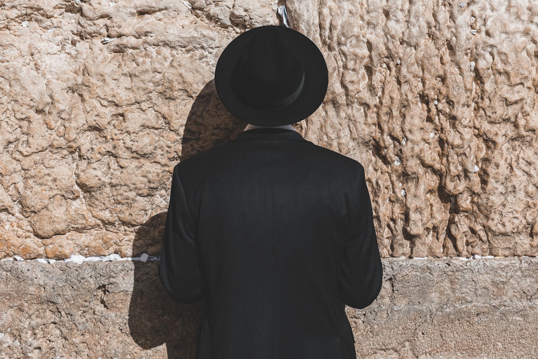 a man wearing a black hat standing in front of a stone wall