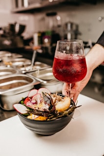 red wine in clear wine glass beside bowl full of food