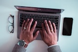 man using laptop between eyeglasses and iPhone
