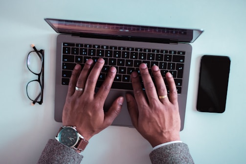 man using laptop between eyeglasses and iPhone