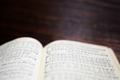 An open book displaying sheet music with musical notes and symbols on a wooden surface. The background is blurred, emphasizing the focus on the pages.