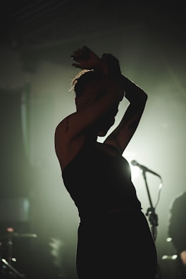 A moody black-and-white still from a music video showing a silhouette against dramatic lighting.