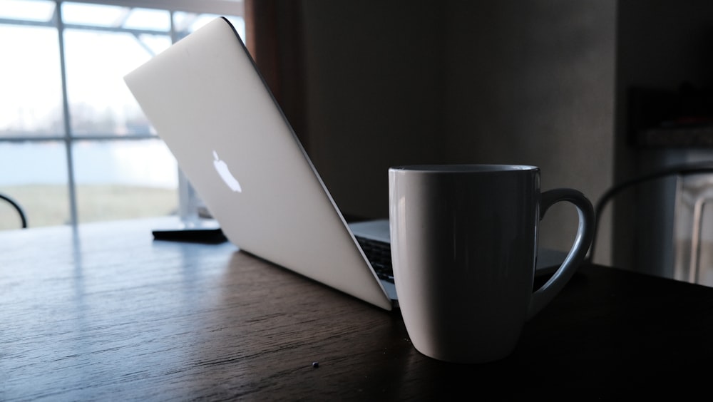 white ceramic mug beside opened Macbook on table