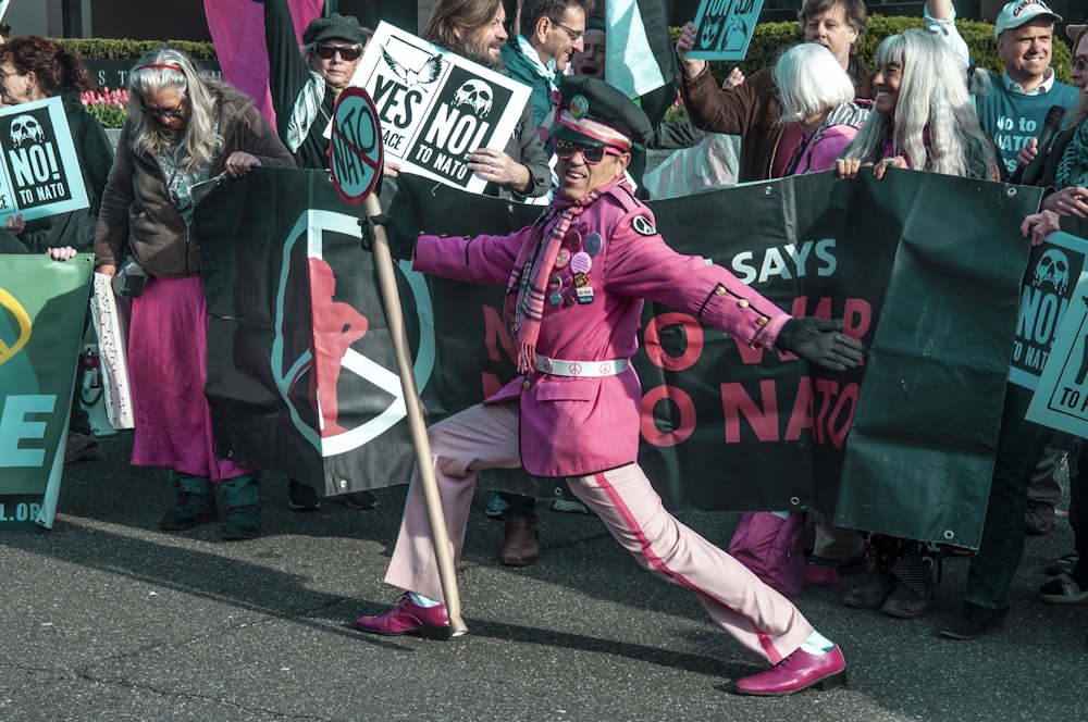 man in pink coat holding sign in front of card holding signs