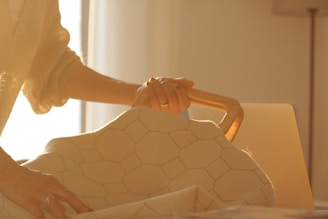A person gently holding a bag with a wooden handle. The fabric of the bag features a hexagonal pattern. Soft, warm lighting casts an amber glow over the scene, suggesting a cozy, serene environment.