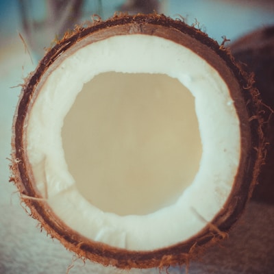 A halved coconut with the inner white flesh and outer brown shell clearly visible. The texture of the coconut fibers is evident around the edges of the shell.