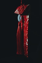 A decorative hanging ornament featuring a red tassel and a jade piece is suspended against a dark background. The ornament's intricate design is illuminated with a red hue, casting dramatic shadows.