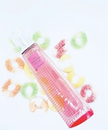 A pink Givenchy perfume bottle labeled 'Live Irresistible Rosy Crush' is placed on a white background, surrounded by colorful sugar-coated gummy rings in shades of green, orange, yellow, and red.