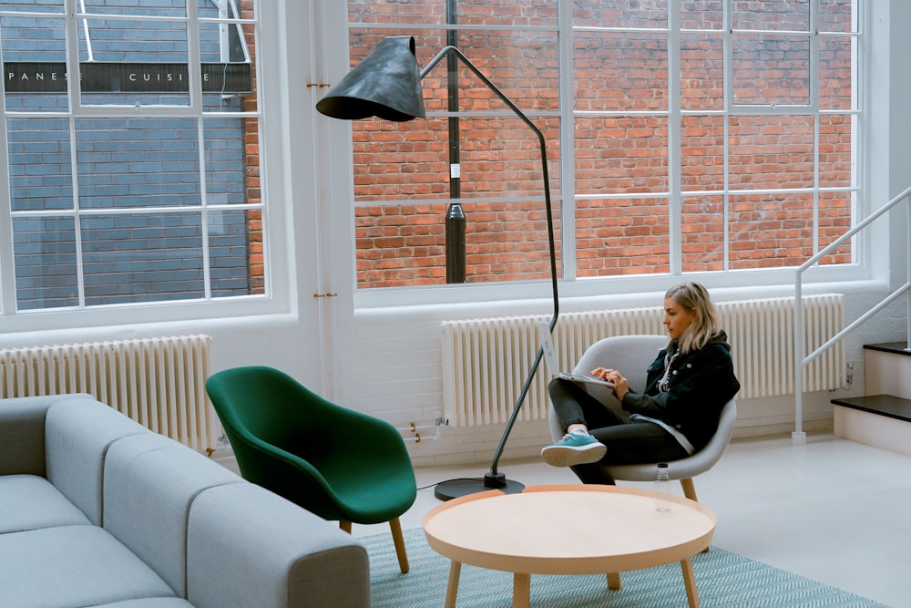 woman sitting on gray padded chair beside round brown coffee table