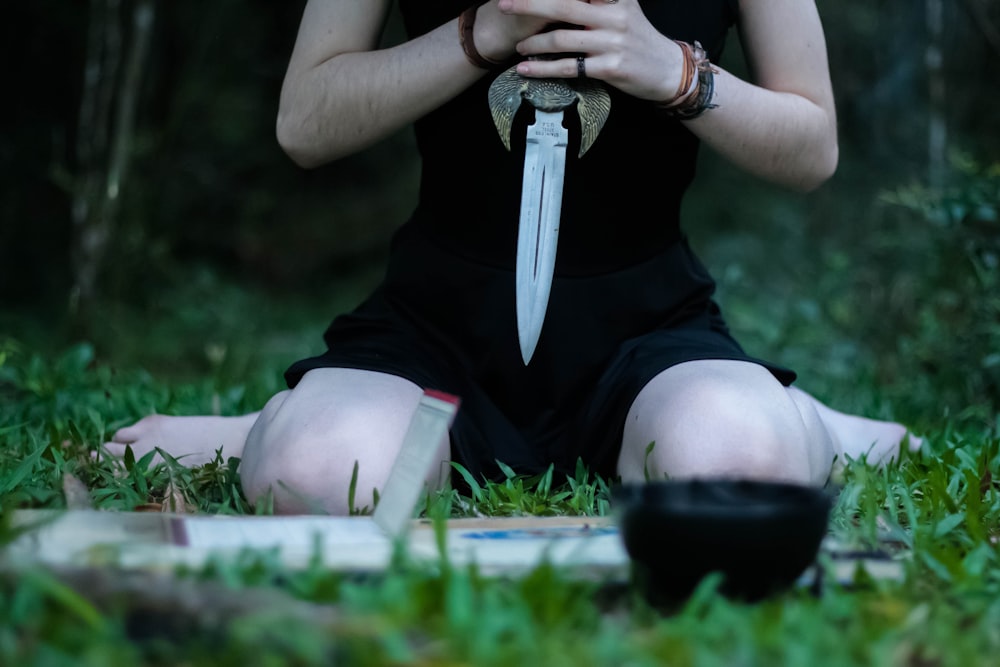 Mujer arrodillada sobre la hierba sosteniendo un cuchillo