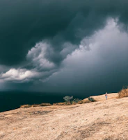 A lone figure standing on cracked earth, gazing at a distant horizon where dark clouds swirl ominously.