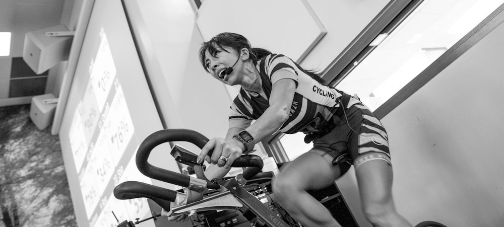 Photographie en niveaux de gris d’une femme sur un vélo elliptique