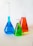 Close-up of laboratory glassware filled with colorful chemical solutions on a white surface.