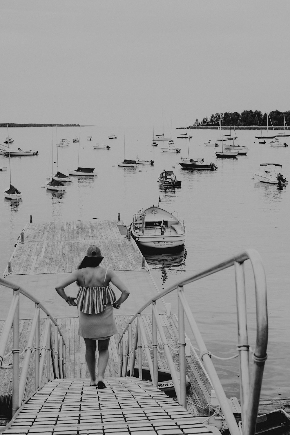 donna che cammina sul molo di metallo vicino allo specchio d'acqua nella fotografia in scala di grigi