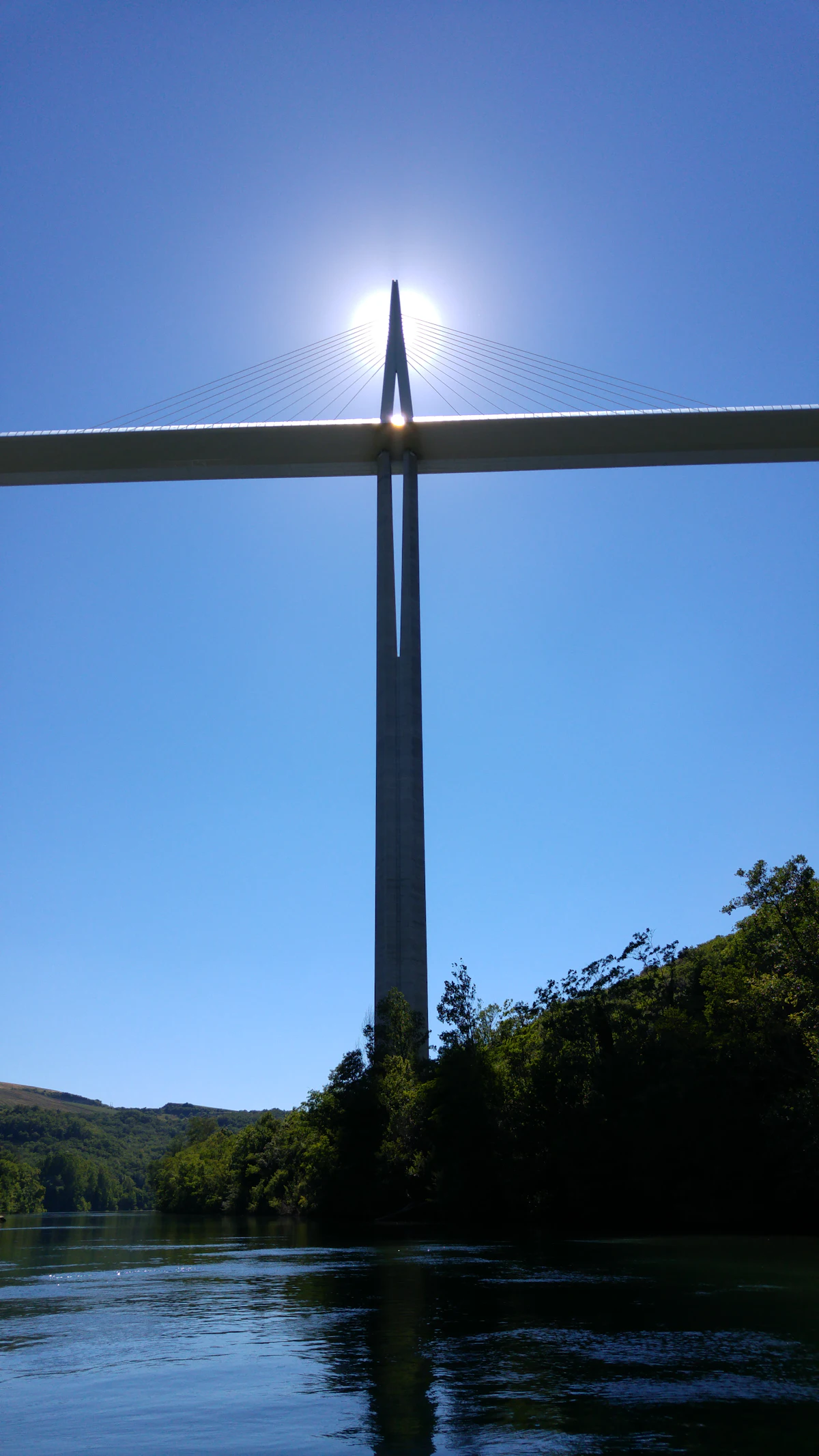 A pylon of the Millau Viaduct rising above the Tarn river and its wooded banks