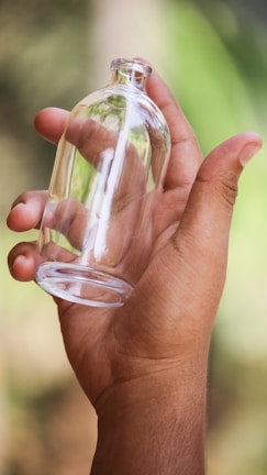 Close-up of a hand holding a glass bottle of organic facial oil with fresh herbs around.