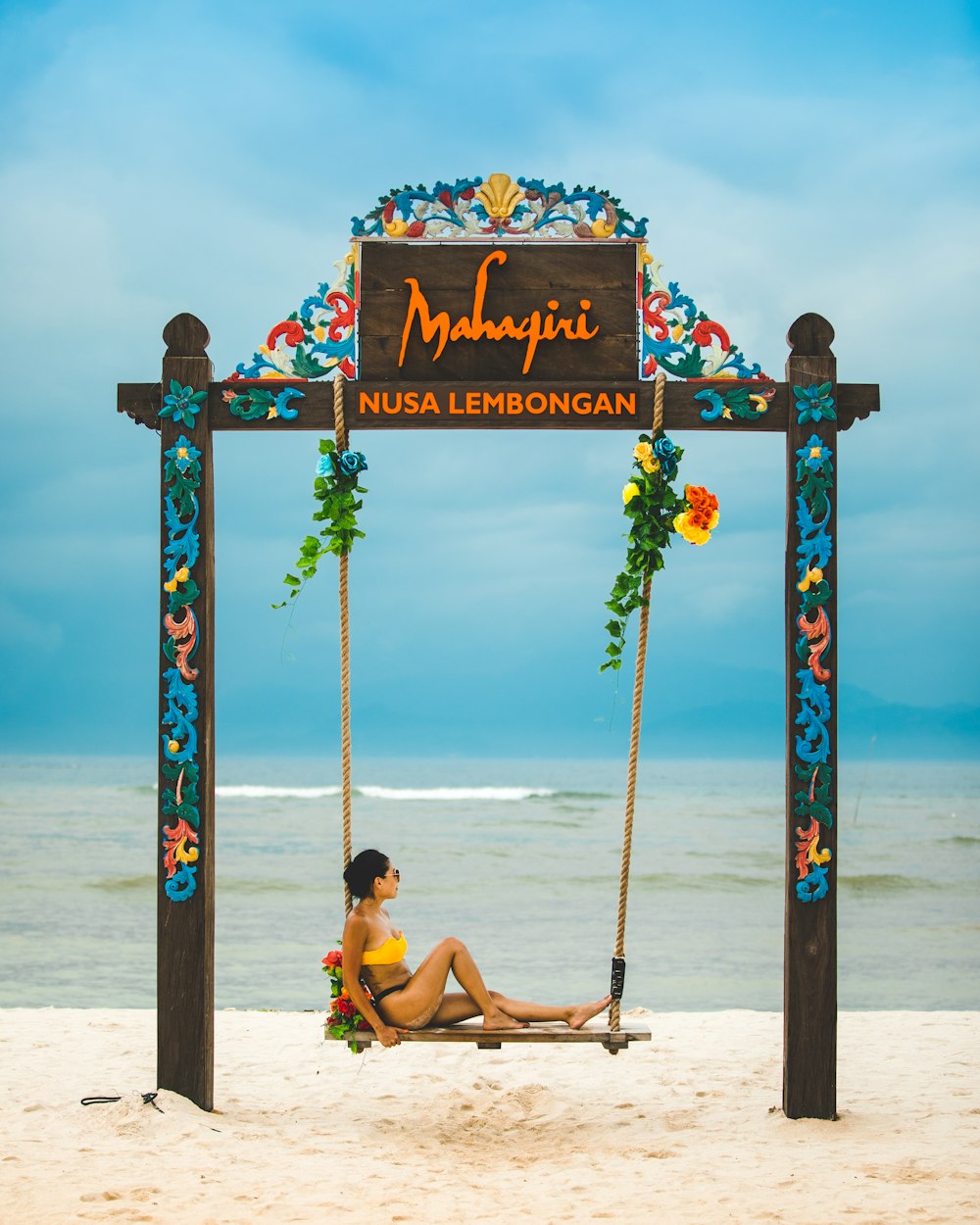 woman sitting on wooden hammock beside sea