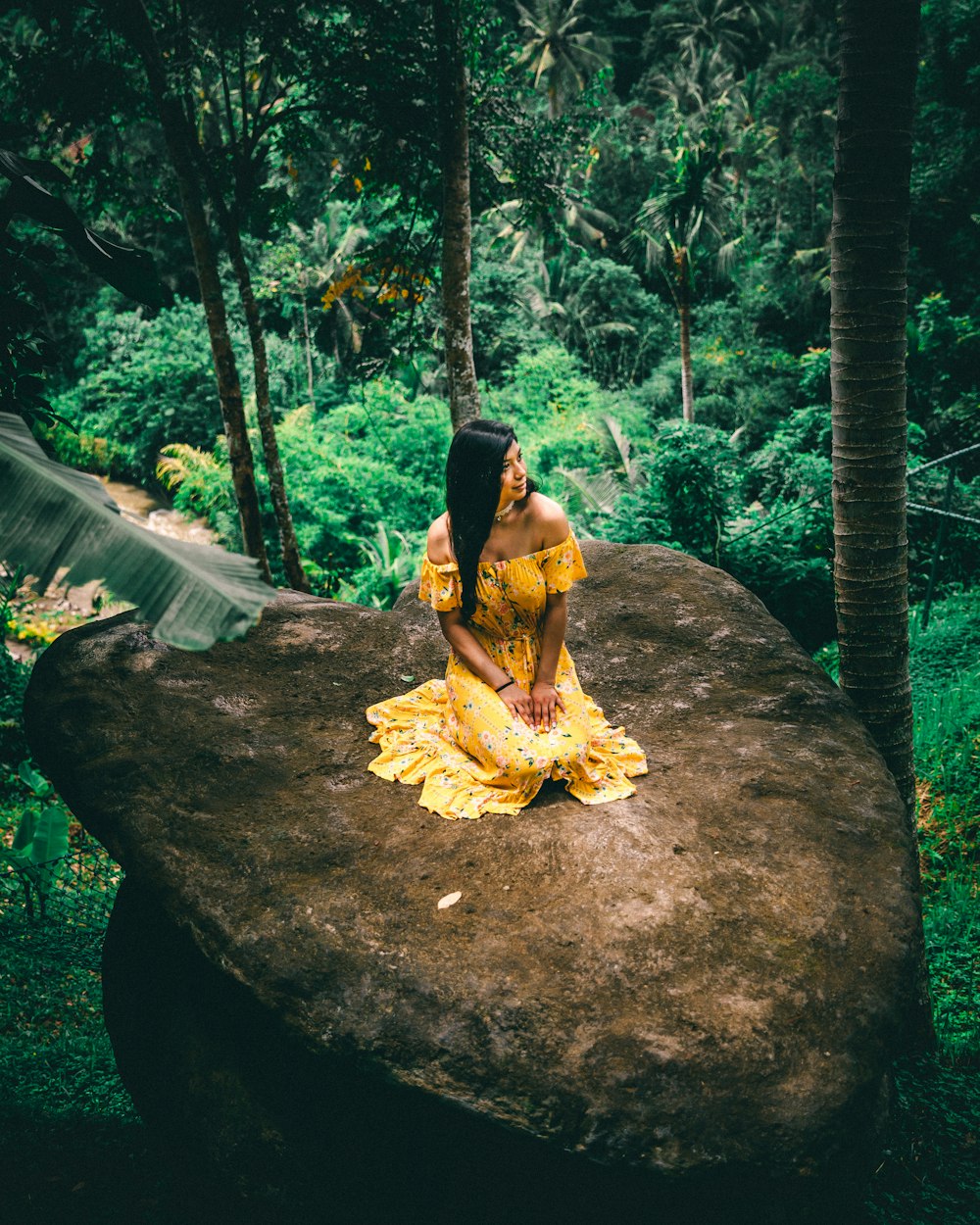 Mujer en vestido floral amarillo arrodillada en la roca