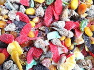 A colorful assortment of dried fruits with various textures, including slices of red, purple, yellow, and green pieces along with nuts and brown wrinkled fruit.