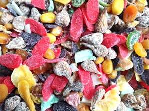 A colorful assortment of dried fruits with various textures, including slices of red, purple, yellow, and green pieces along with nuts and brown wrinkled fruit.