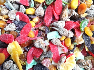 A colorful assortment of dried fruits with various textures, including slices of red, purple, yellow, and green pieces along with nuts and brown wrinkled fruit.