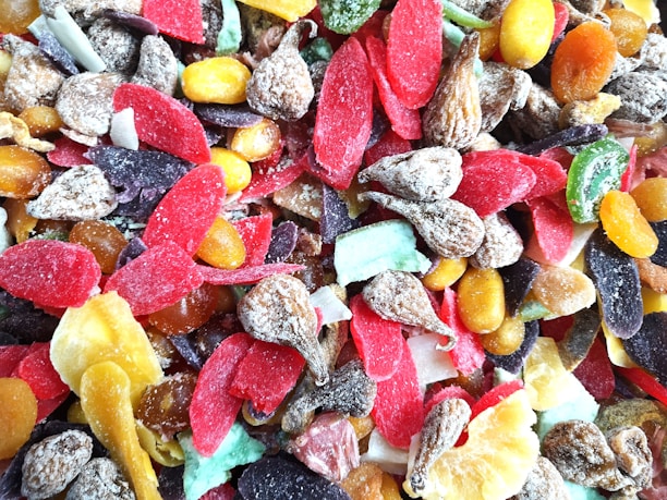 A colorful assortment of dried fruits with various textures, including slices of red, purple, yellow, and green pieces along with nuts and brown wrinkled fruit.
